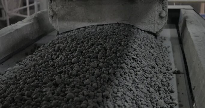 A lot of gray pebbles on the transporter in factory. Location not relevant. A lot of rocks on conveyor. A lot of stones on conveyer. Cement making