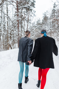 beautiful young stylish couple of girls in vintage clothes with blazer and tights run through the winter forest with snow. Extraordinary love and friendship concept. Youth feminine style.