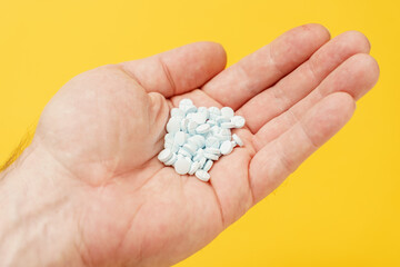 a lot of blue tablets in man's hand on yellow background