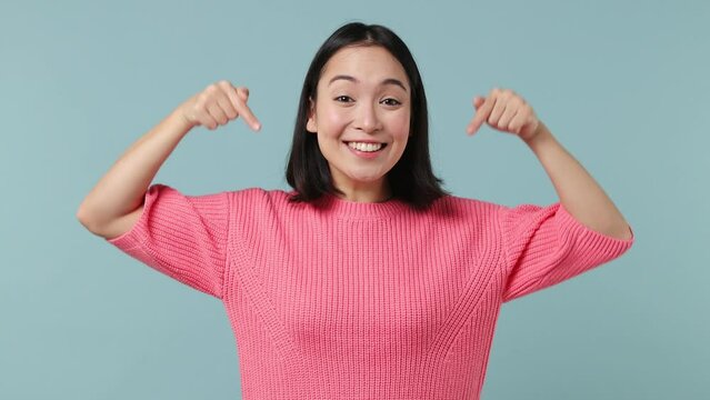 Smiling happy young woman of Asian ethnicity 20s years old wears pink shirt pointing fingers down on workspace area copy space mock up isolated on plain pastel light blue background studio portrait