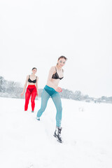 Two vogue girls in colorful tights and bras run in a winter field with snow. creative clothing style