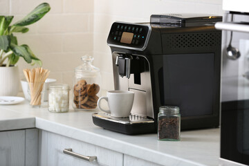 Modern electric coffee machine with cup on white countertop in kitchen