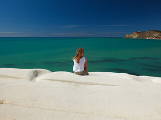 Young woman sitting at the top of Scala dei Turchi in Sicily with a nice view of green sea