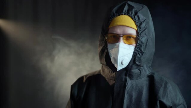 A man in a black medical chemical protection suit and a white respirator, wearing yellow glasses, a yellow hat and black medical gloves shows a middle finger gesture, and then delivers boxing punches