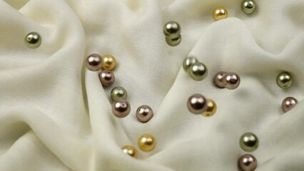 Big pearl beads different colors fall on a white textile, gathered into soft folds, background, slow motion