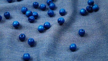 Big wooden blue beads fall on the blue denim, background, slow motion