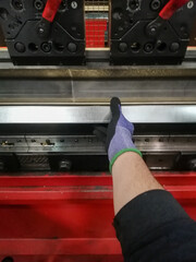vertical close-up of a hand working on a metal bending machine gripping a part while it is being...