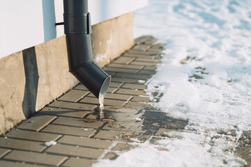 downpipe on a house building in winter with an icicle sticking out of the pipe and snow on the background