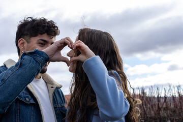 Affectionate young mixed race couple laughing and making heart shapes with their hands while standing outdoors