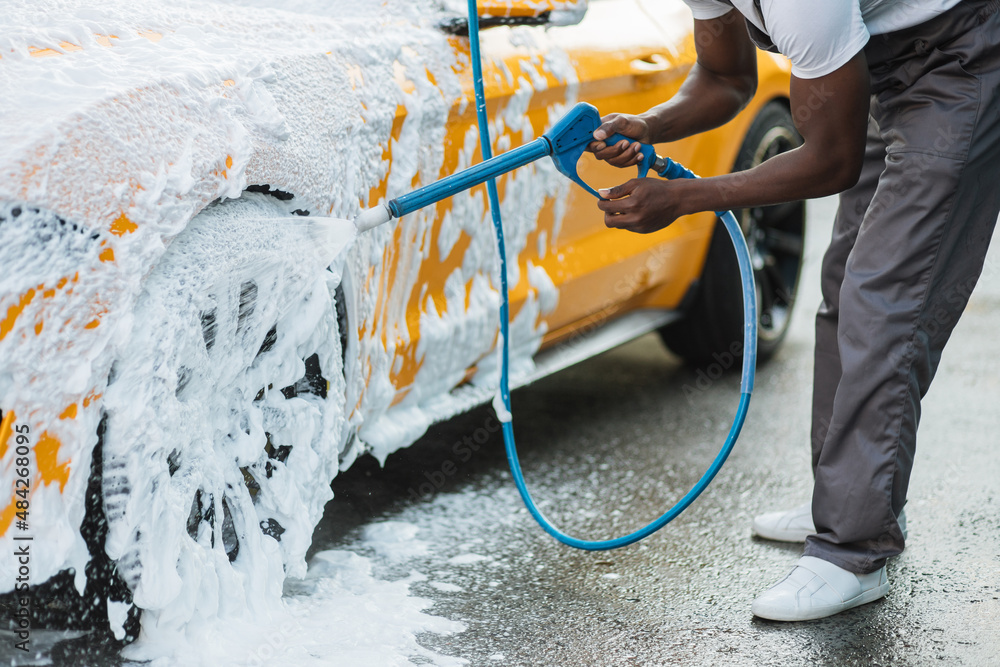 Poster Car washing outdoors. Crop close up of car washing high pressure foam. Wheel alloy cleaning at car wash station with high pressure foam. Washing rims.