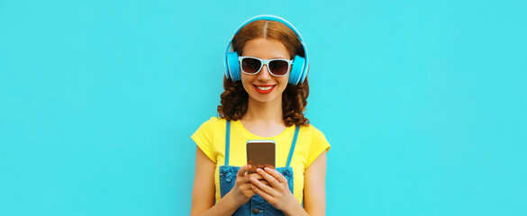 Fototapeta na wymiar Portrait of happy smiling young woman in headphones listening to music with phone on blue background
