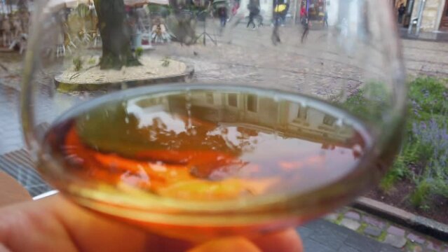 A glass of cognac in front of a busy city square.