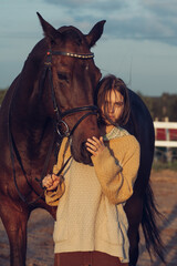 A young girl with a short haircut next to her horse at sunset. Good friends. Summer and happiness.