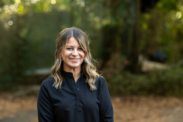 A young cosmetologist standing outside among green trees for a headshot with copy space