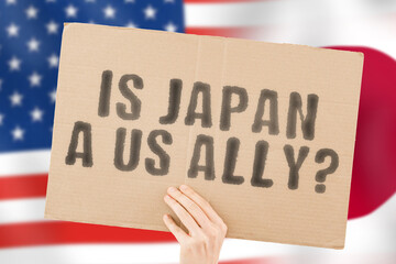 The question " Is Japan a US ally? " on a banner in men's hand with blurred American and Japanese flag on the background. Union. Togetherness. Conclusion. Confrontation. Report. Global