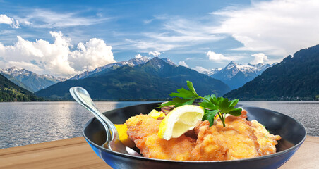 Traditional austrian food (Wiener schnitzel) against Zell am see village with lake in Austria