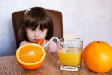 Portrait of a little girl plays with an oranges on a table. Selective focus of orange fruit