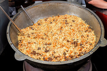 Cooking of traditional pilaf in big cauldron on food market, national cuisine, street food in outdoor