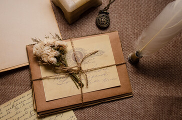 Photo in retro style. Craft envelopes and old letters tied with jute thread and decorated with dried flowers, an old clock lies nearby.