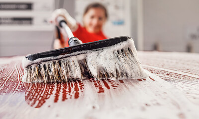 Closeup detail on white soap foam and brush with suds moving over roof as young woman cleans her...