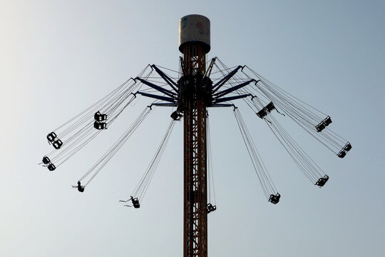 Unidentified people riding on spinning swing carousel in amusement park. Entertainment concept - High spinning swing carousel against blue sky. Motion blur