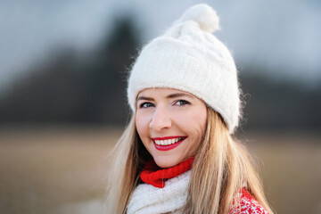 Portrait of young woman in white winter hat and red jumper, closeup to her smiling face