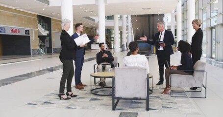 He's setting his team up for success. Diverse businesspeople having a discussion in a convention centre office lobby. Confident happy colleagues talking and planning for meeting and conference  - Powered by Adobe