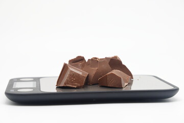 Large broken pieces of milk chocolate on an electronic kitchen scale.