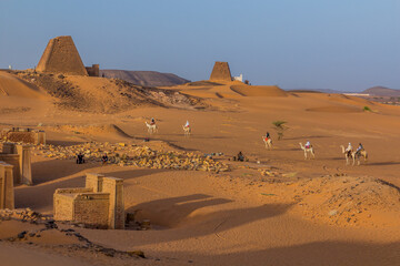 MEROE, SUDAN - MARCH 4, 2019: Locals on camels near Meroe pyramids, Sudan - obrazy, fototapety, plakaty