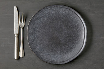 Dark plate on a dark concrete background with cutlery