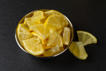 Fresh cutted lemon slices in a metal bowl on a black slate slab. Sliced yellow citrus for vitamin C, antioxidant, healthy eating and cooking concepts. Sour lemon fruit.