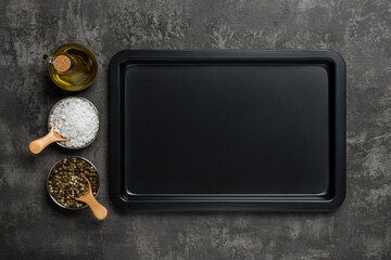 Empty baking sheet, olive oil jar, salt and pepper grains over black textured background....