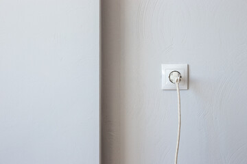 Plug with a cord in an electrical outlet against a gray wall with copy space. Electricity consumption