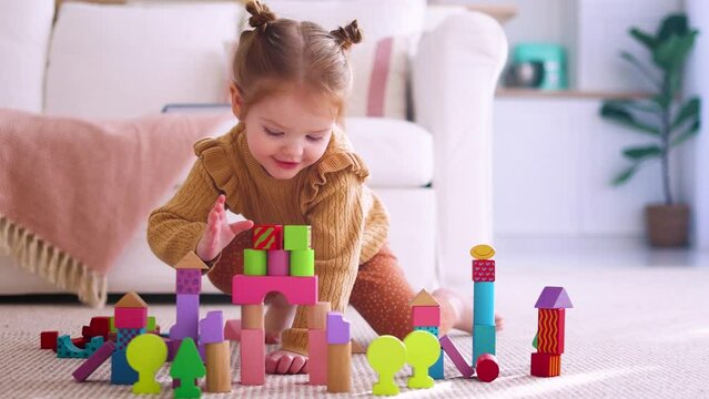 cute little baby is playing the colorful wooden blocks, building a toy castle on the carpet at home on sunny day
