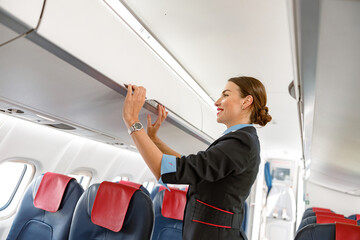 Joyful stewardess closing overhead luggage bin in airplane