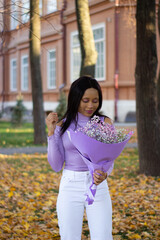 A beautiful African lady wearing a purple top outfit holding a flower in a park.