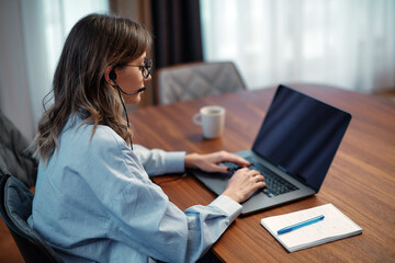 Female call center agent operator in headset ready to accept video call looking at laptop, sit at desk. Customer service
