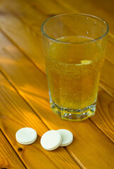 Glass with a sizzling liquid and round tablets . Taking vitamins. Vertical photo.