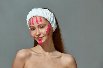 Beautiful redhead young girl with bare shoulders, face lift tapes on face enjoy facelifting...