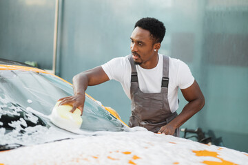 Young attractive African American man washing his yellow luxury car in a self-service car wash...