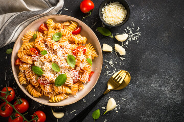 Traditional Italian pasta with tomato sauce, basil and parmesan on black table. Fusilli pasta with tomato sauce arrabbiata. Top view.