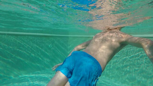 Preteen boy in underwater while relaxing at swimming pool. Child body tempering through thermal environment techniques. Improves the immune system function during summer vacations.
