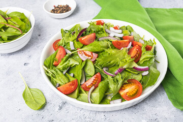 Summer green salad in white bowl plate on grey table