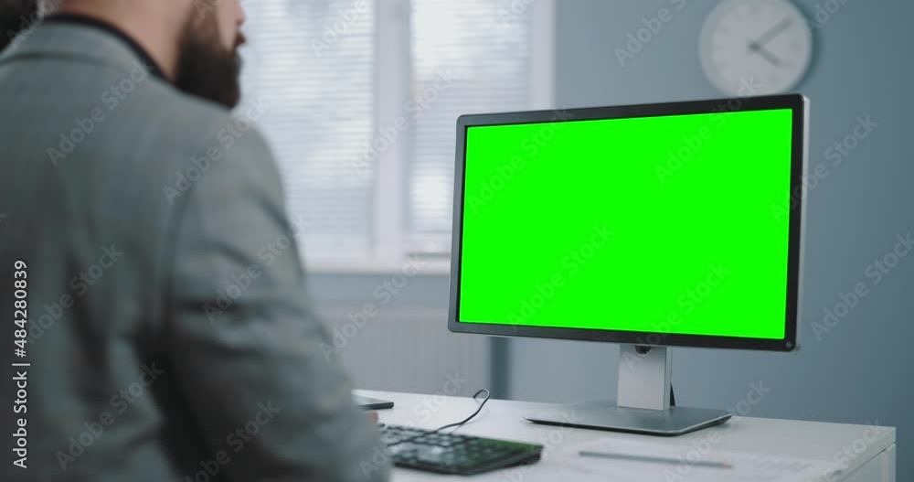 Poster view from shoulder of mature businessman using modern pc with green mock up screen while working at 