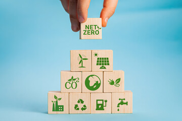 Net zero and carbon neutral concept. Net zero greenhouse gas emissions target. Climate neutral long term strategy. Hand put wooden cubes with green net zero icon and green icon on grey background. - obrazy, fototapety, plakaty