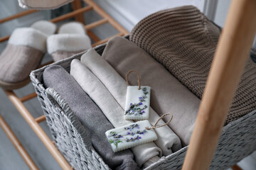 Beautiful scented wax sachets and folded clothes in wicker basket on rack indoors