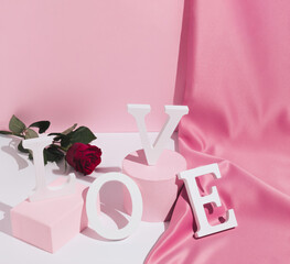 Romantic pastel pink Valentine's Day composition with word Love, satin curtain and red rose flower. Modern aesthetic. Minimal love concept.