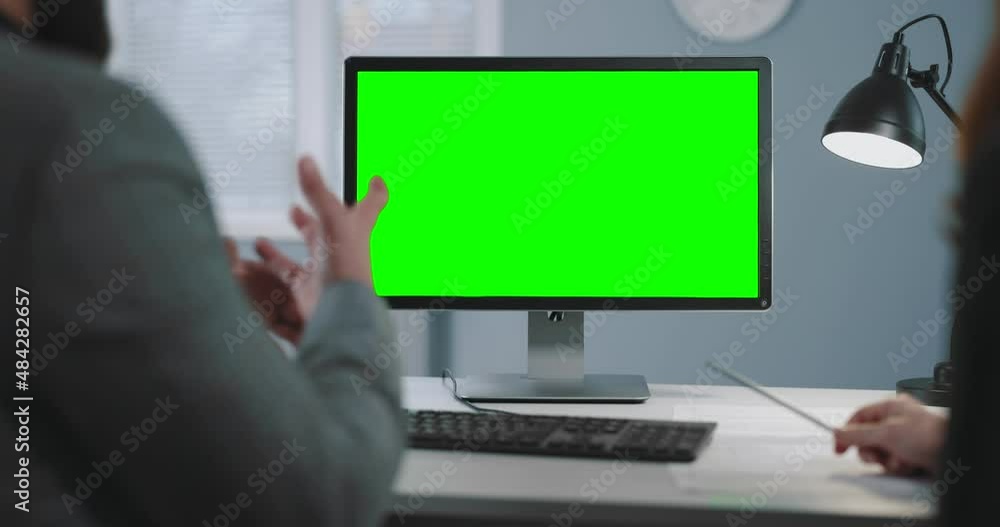 Poster back view of two business partners looking computer with green mock up screen while sitting together