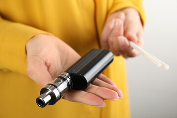 Woman with cigarettes and vaping device on light background, closeup. Smoking alternative
