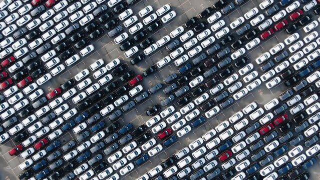 Motion over rows of finished cars of different colours at huge open warehouse ground of giant plant bird eye view, giant car parking